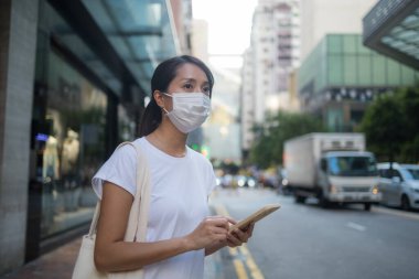 Yüz maskesi takan kadın telefondaki konumunu kontrol ediyor.