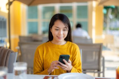 Kadın restoranın dışında otururken telefonu kullanıyor.