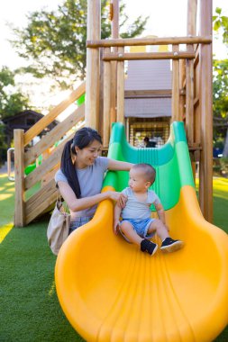 Genç anne Sunny Park 'ta bebekle oyun parkında eğleniyor.