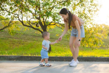 Anne küçük oğlunu gün ışığında parkta taşıyor.