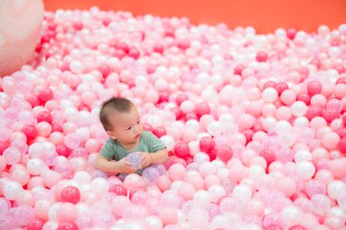 Bebek pembe top havuzunda mutlu bir şekilde oynuyor.