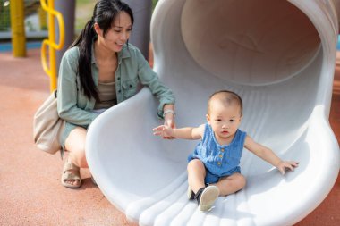 Anne ve bebek park kaydırağında mutlu bir şekilde kayıyor.