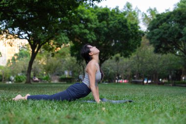 Yukarı doğru köpek yogası yapan bir kadın park yerinde poz veriyor.