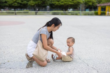 Anne, dışarıdaki parkta peçeteyle bebek elini siliyor.
