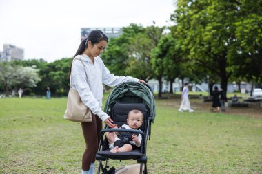Anne küçük bebekle parkta bebek arabasında yürüyor.