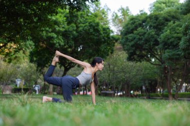 Yeşil parkta yoga yapan bir kadın.