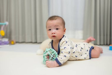 Yeni doğmuş bebek yerde yatıp oyuncakla yukarı bakıyor.