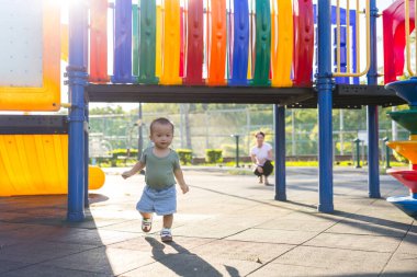 Anne arkasını kollarken bebek parkta oynuyor.