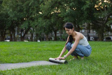Yeşil park çimlerinde yoga minderi yuvarlayan kadın.