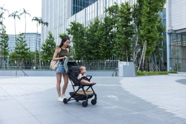 Anne küçük bebekle birlikte şehir caddesinde bebek arabasında yürüyor.