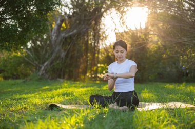 Çimlerin üzerinde otururken akıllı saati kontrol eden kadın
