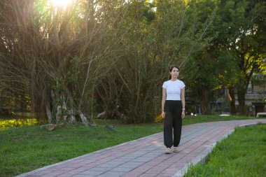 Yeşil güneşli parkta tek başına yürüyen bir kadın