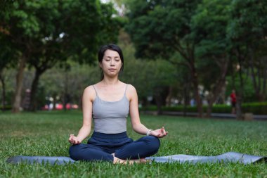 Genç bir kadın çimenlerde oturmuş, açık havada derin nefes alıyor.