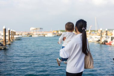 Anne kucağında bebek, sakin deniz ufkunu seyrediyor.