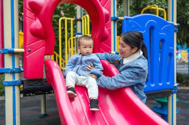 Anne bebeğini parkta sürgülü oynamaya götürüyor.