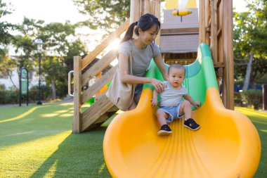 Anne rengarenk oyun parkında bebeğe yardım ediyor.