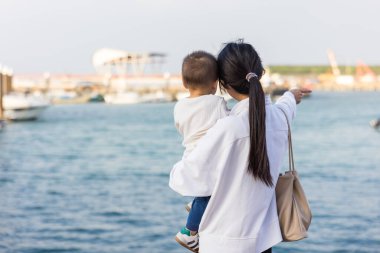 Anne okyanus manzarasını izlerken bebeği tutuyor.