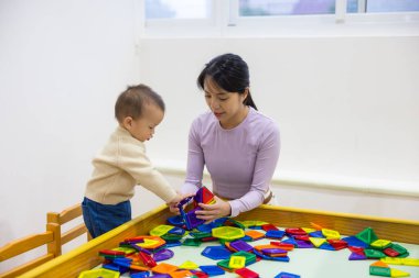 Anne bebeğine renkli mıknatıs kulesi yapımında yardım ediyor.