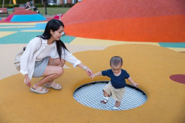 Renkli parkta annesiyle oynayan bir bebek.