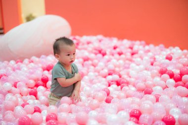 Tatlı bebek top havuzunda oturuyor ve oynuyor.