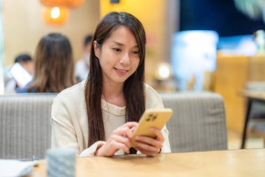 Restoranda otururken cep telefonu kullanan bir kadın.