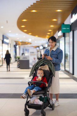 Anne, alışveriş merkezindeki bebek arabasında süt içen bebekle telefonu kontrol et. 