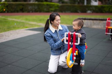 Anne oğluyla parkta sallanan sandalyede oynuyor.