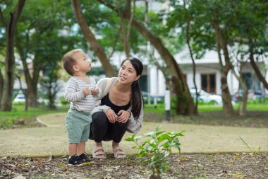 Anne, yeni yürümeye başlayan bebekle birlikte dışarıda doğayı gözlemliyor.