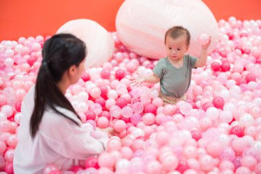 Anne top havuzunda bebekle oynuyor.