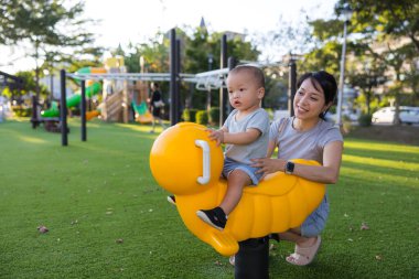 Anne parkta sallanan sandalyede bebekle oynuyor.
