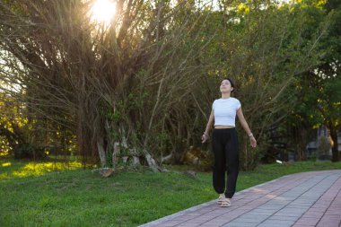 Kadın parkta yürürken temiz hava soluyor.