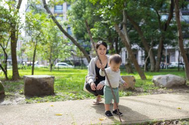 Anne, ufaklığın dışarıda sopayla oynamasını izliyor.
