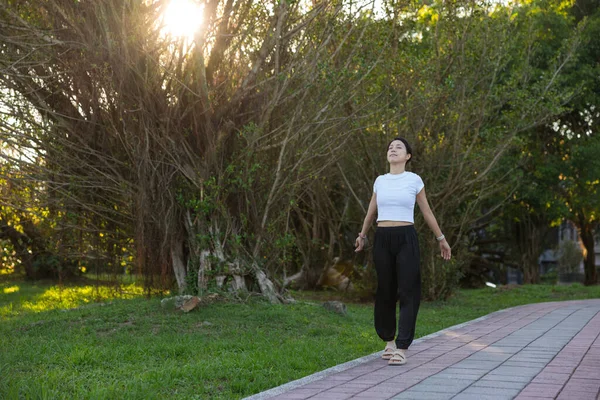 Kadın parkta yürürken temiz hava soluyor.