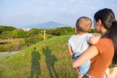 Anne kucağında bebekle otların üzerindeki gölgelere bakıyor.