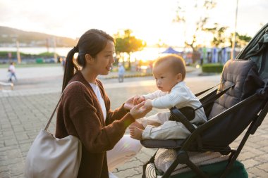 Anne gün batımında bebek arabasının yanında elini tutuyor.