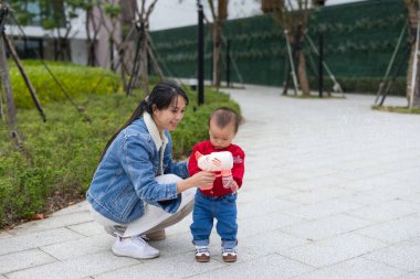 Anne oğluna balon makinesi oynamayı öğretiyor.