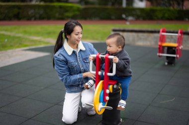 Anne, bebeği parka sallanan sandalyeye götür.