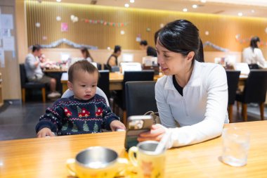 Bebek ve anne restoranda yemek yerken telefon izliyor.
