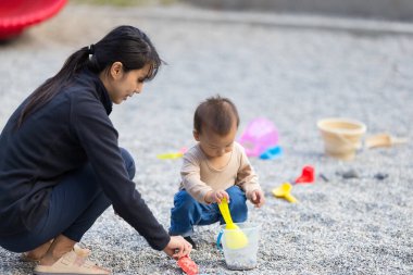 Anne dışarıda bebekle taş kazma oyunu oynuyor.