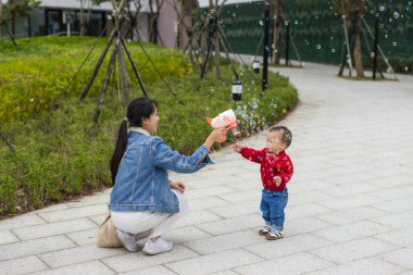 Anne dışarıda bebekle baloncuk oyuncağı oynuyor.