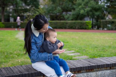 Bebek parkta ekmek yerken annesinin üzerine oturuyor.