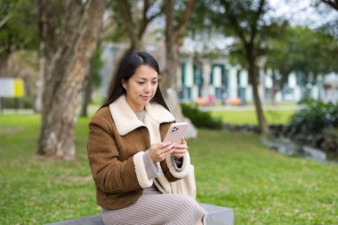 Parkta cep telefonu kullanan genç bir kadın.