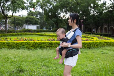 Anne, bebeği taşıyıcı ile parkta taşıyor.