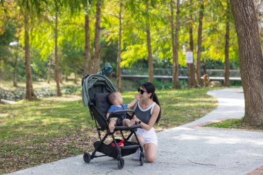 Anne, bebek arabasının orman yolunda bebeğe bakıyor.