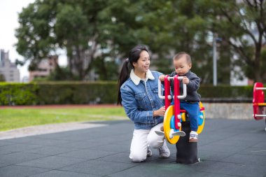 Anne, bebeğin dışarıda sallanan sandalyede oynamasına yardım ediyor.