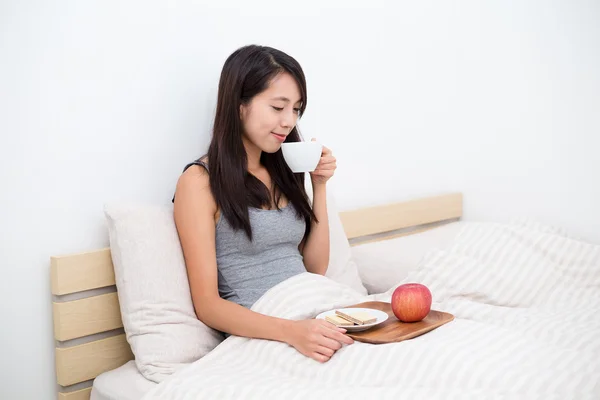 Frau sitzt auf Bett und trinkt Kaffee — Stockfoto