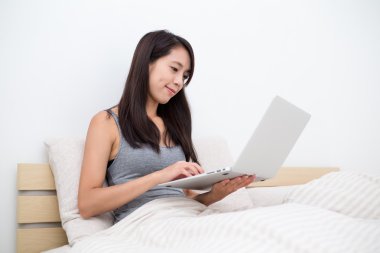 dizüstü bilgisayar kullanarak ve yatağın üstüne oturan kadın