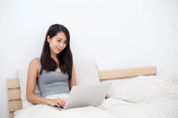 Dizüstü bilgisayar kullanarak ve yatağın üstüne oturan kadın — Stok fotoğraf
