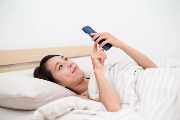 Mulher na cama e usando telefone celular — Fotografia de Stock