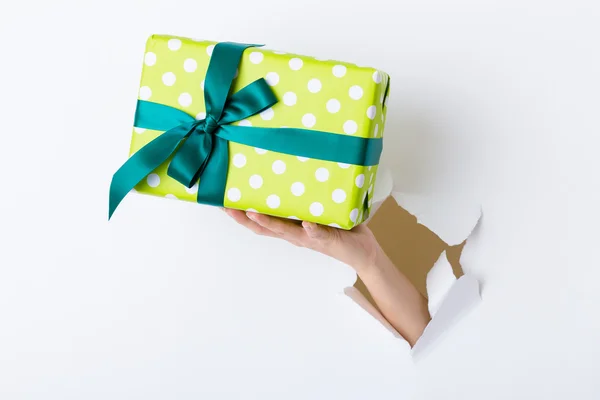 Hand through the hole in paper with present box — Stock Photo, Image